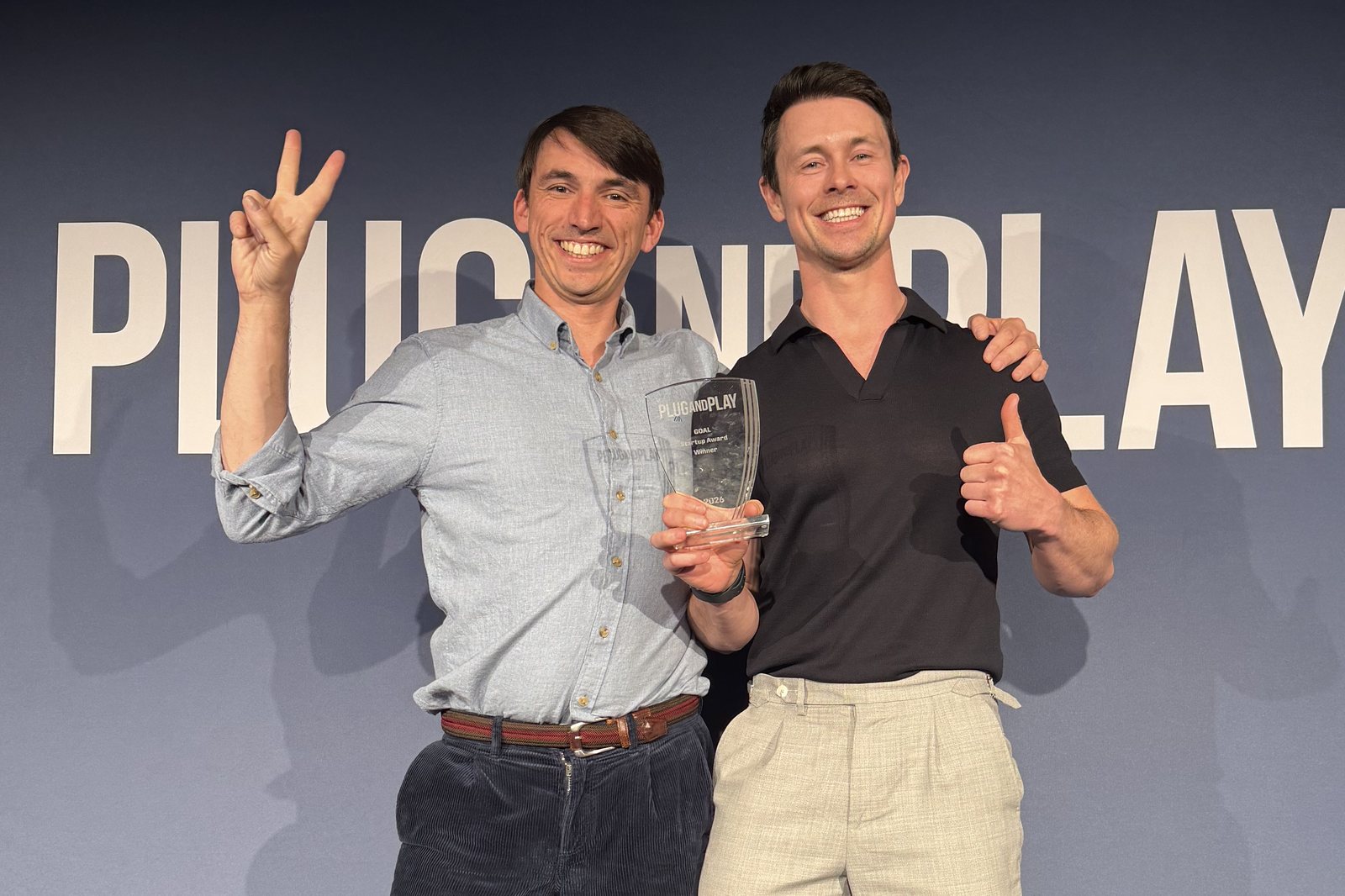 VeriCasa co-founders on stage in front of a Plug and Play backdrop, holding a glass award.